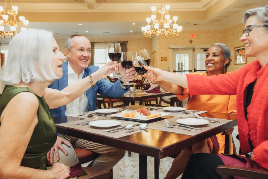 Older adults toasting with glasses of red wine at a dining table under a chandelier