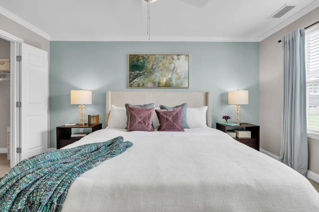 Bedroom with a white bed, a teal blanket at the foot, nightstands with lamps and a framed painting