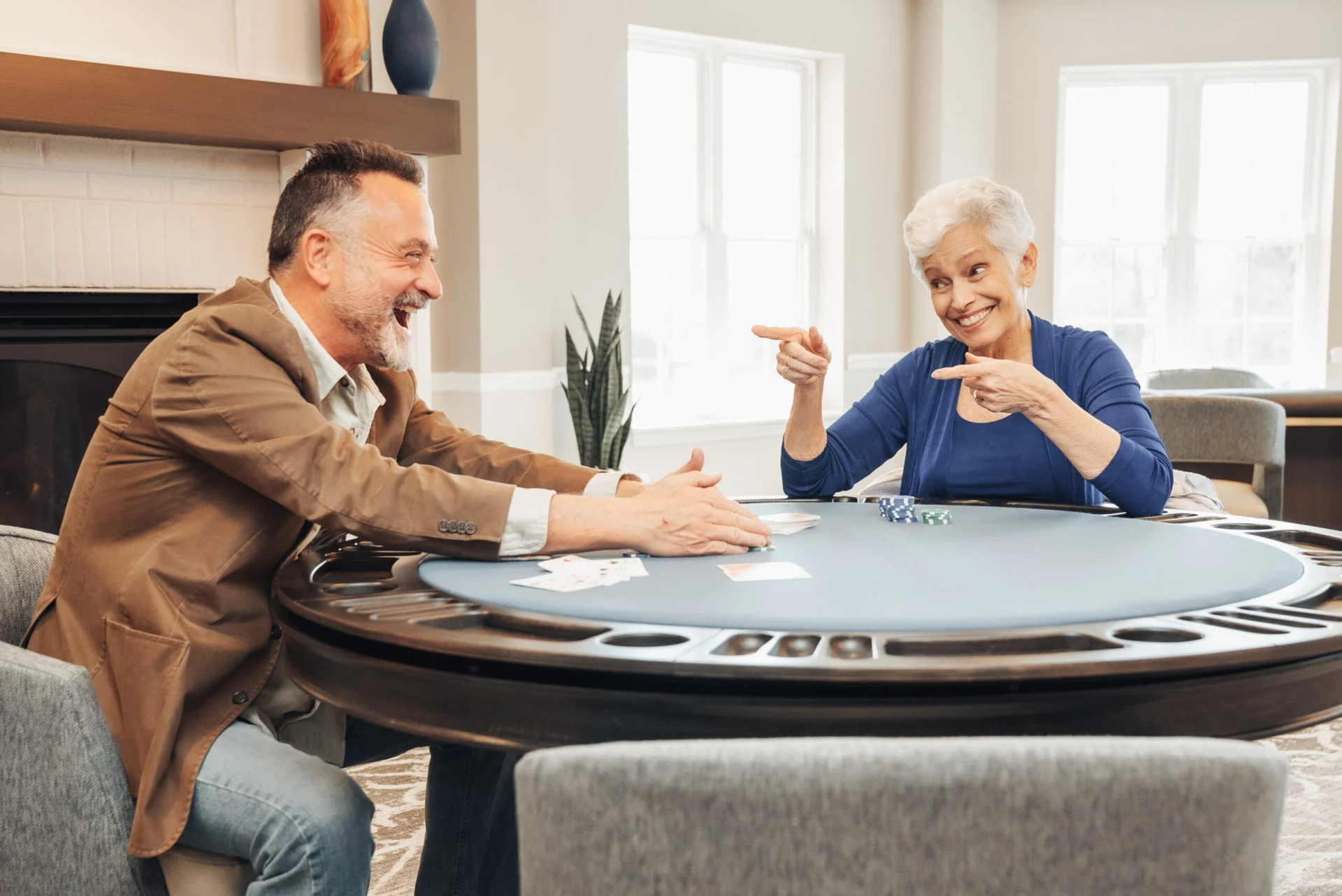 Older man in a brown blazer and an older woman laughing while playing cards at a poker-style table