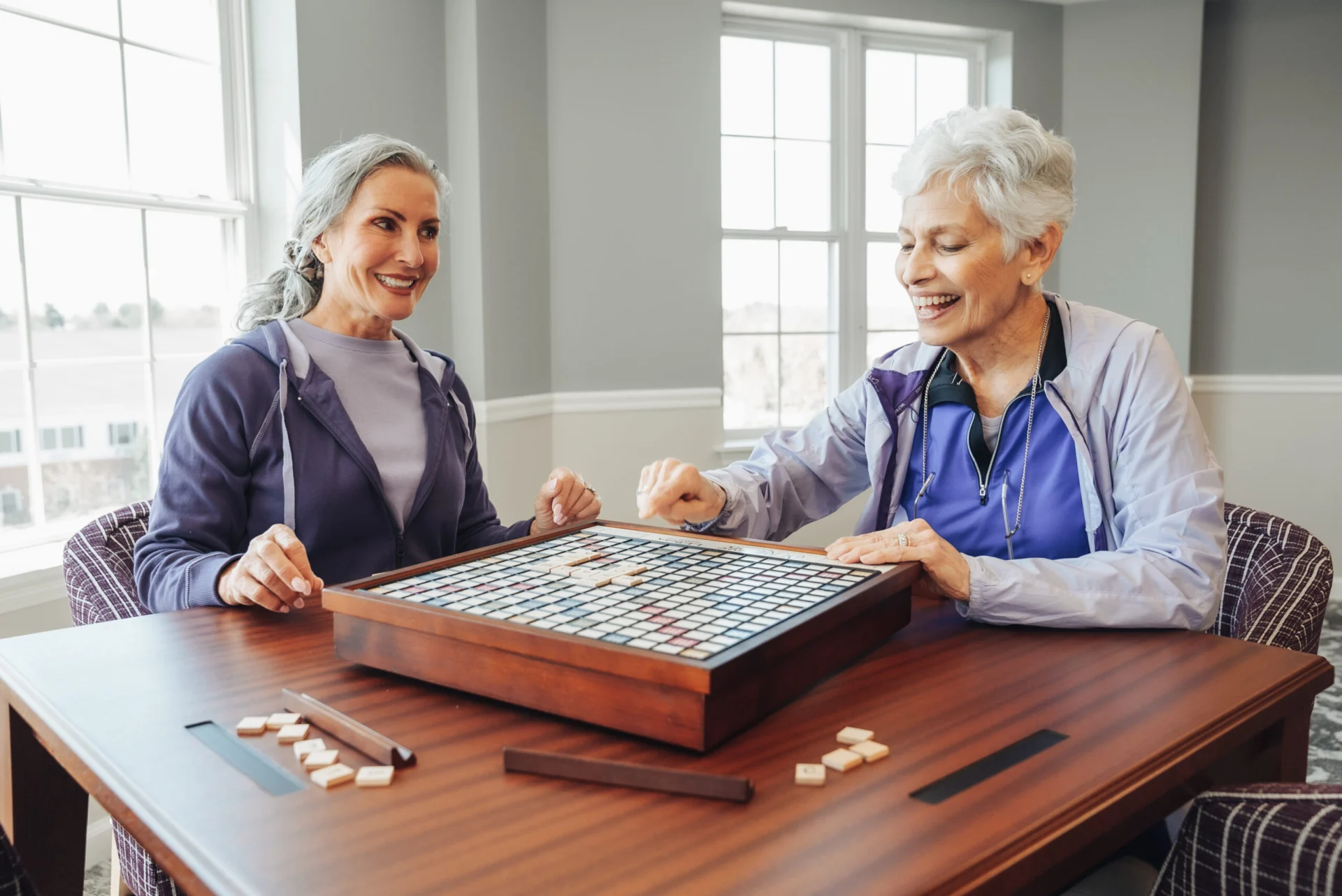Two older women smiling while playing a tile word game at a table