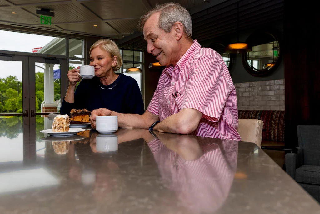 Older man and woman smiling over coffee and pastries at a kitchen counter