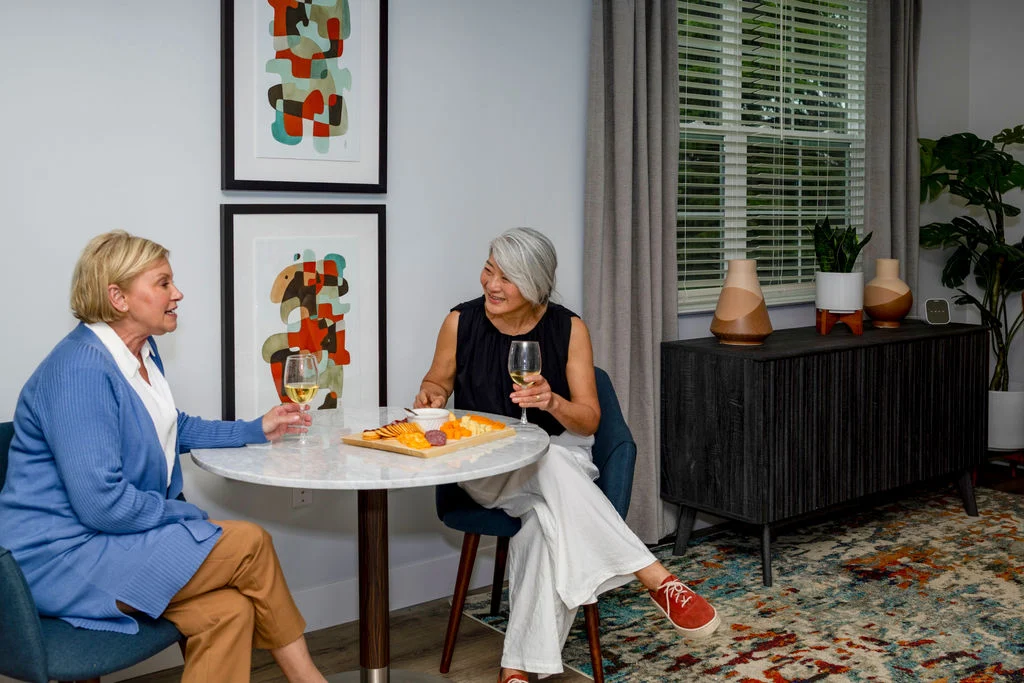Older woman holding a glass of wine and chatting with friends at a table with appetizers