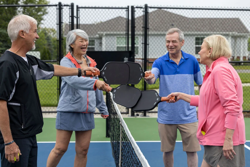 Older adults holding paddles and chatting at the net of an outdoor court