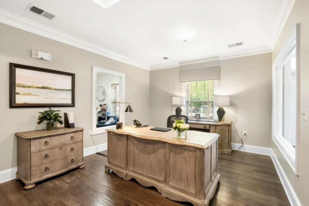 Office with a wooden desk, a credenza, framed art and windows