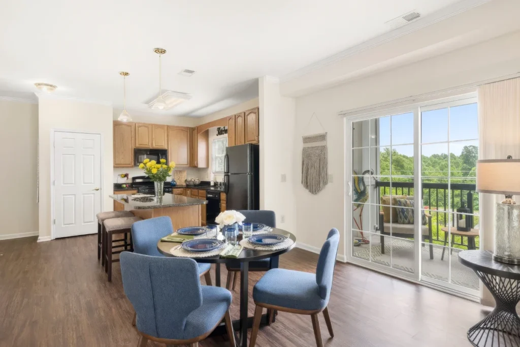 Apartment kitchen and dining area with a round table, blue chairs and a sliding door to a balcony