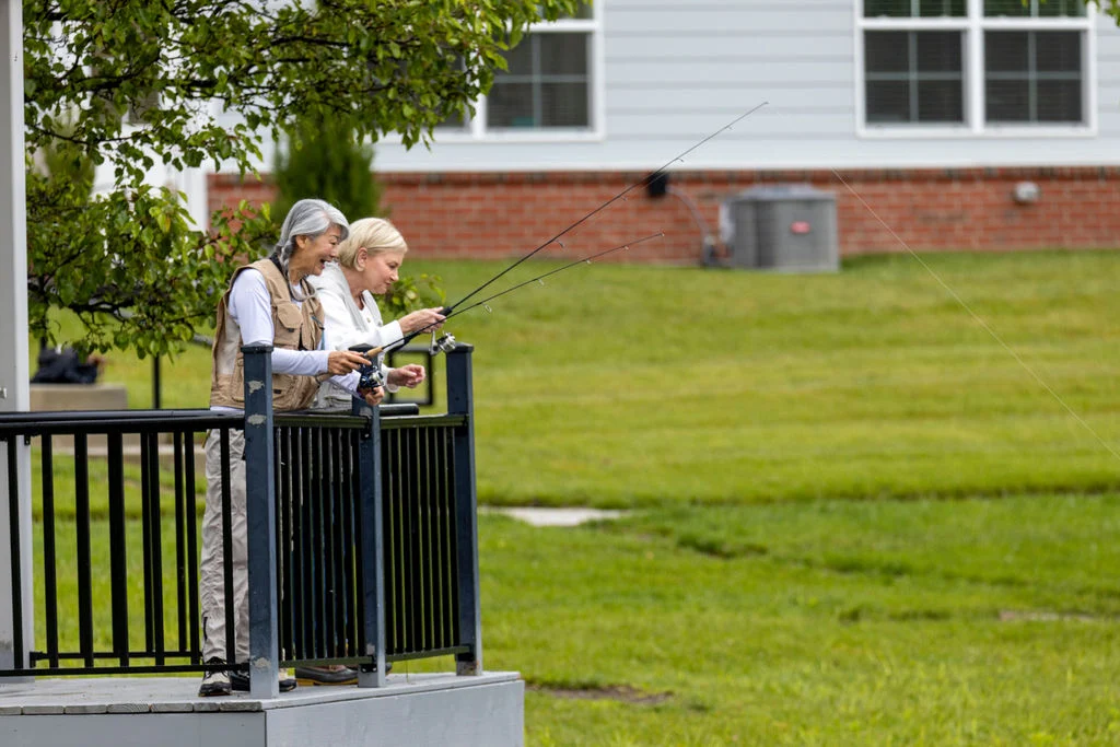 Two older adults standing at a porch railing overlooking a green lawn