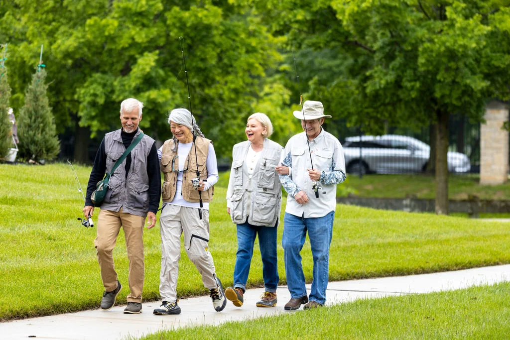Group of four older adults in light jackets walking together across a lawn