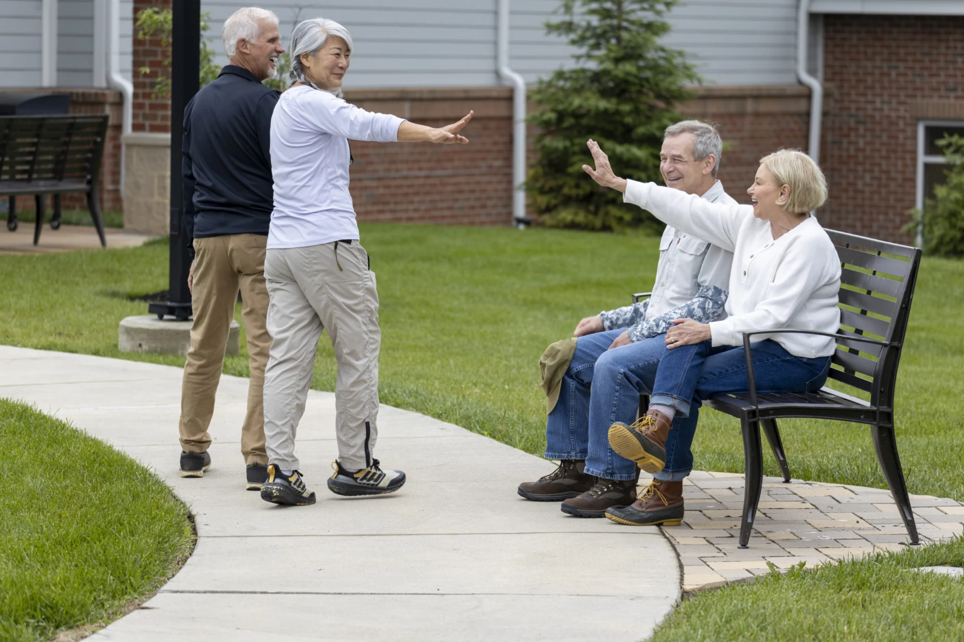 Older adults on a paved walkway, two seated on a bench and two standing, chatting and gesturing outdoors