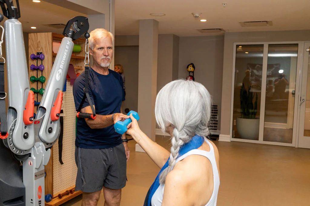 Older man using an exercise machine and an older woman with a long braid in a fitness room