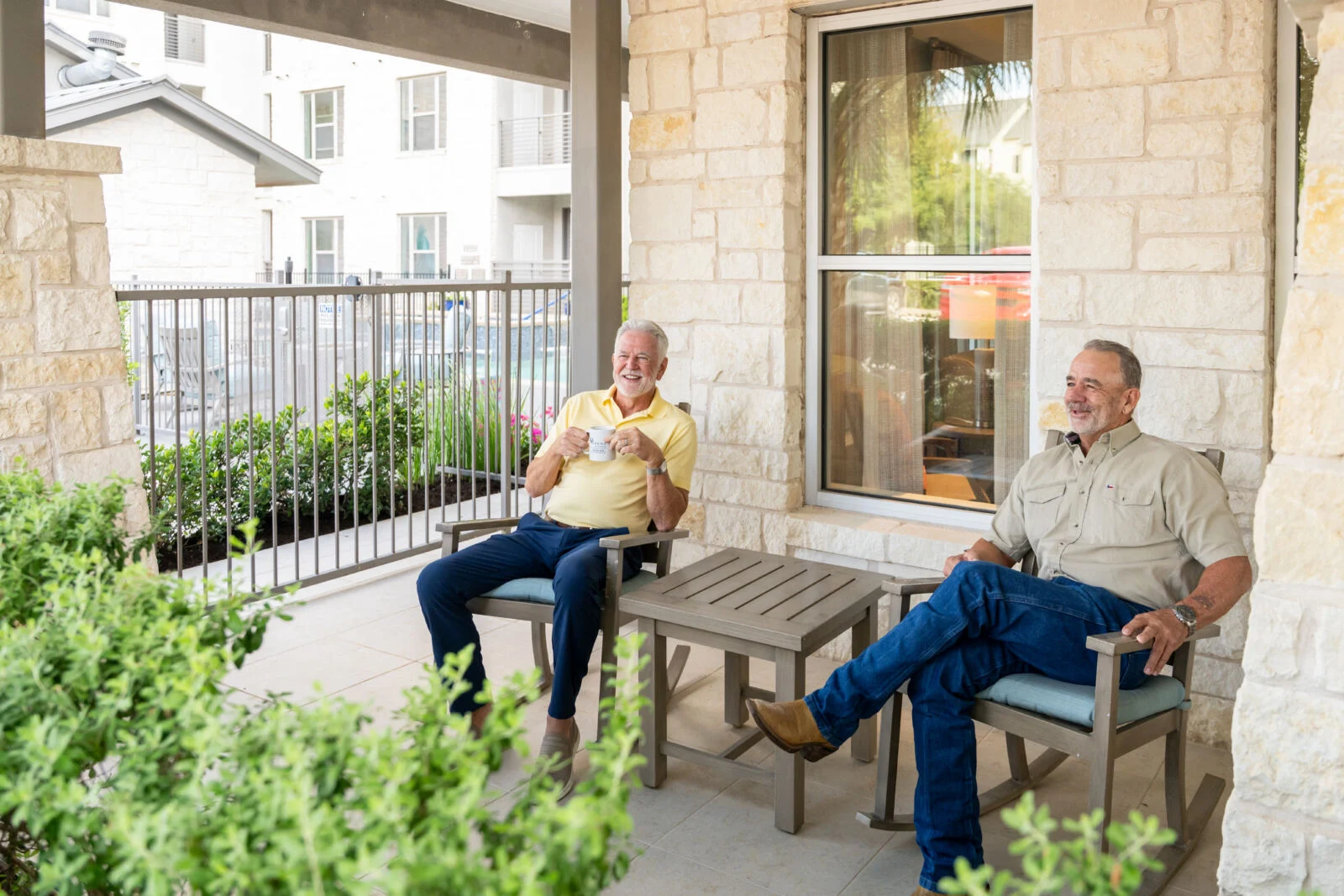 Two older men relaxing in chairs and chatting on a covered stone patio