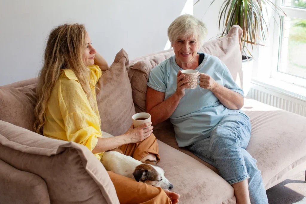 Senior woman having tea with her adult daughter and their dog at home