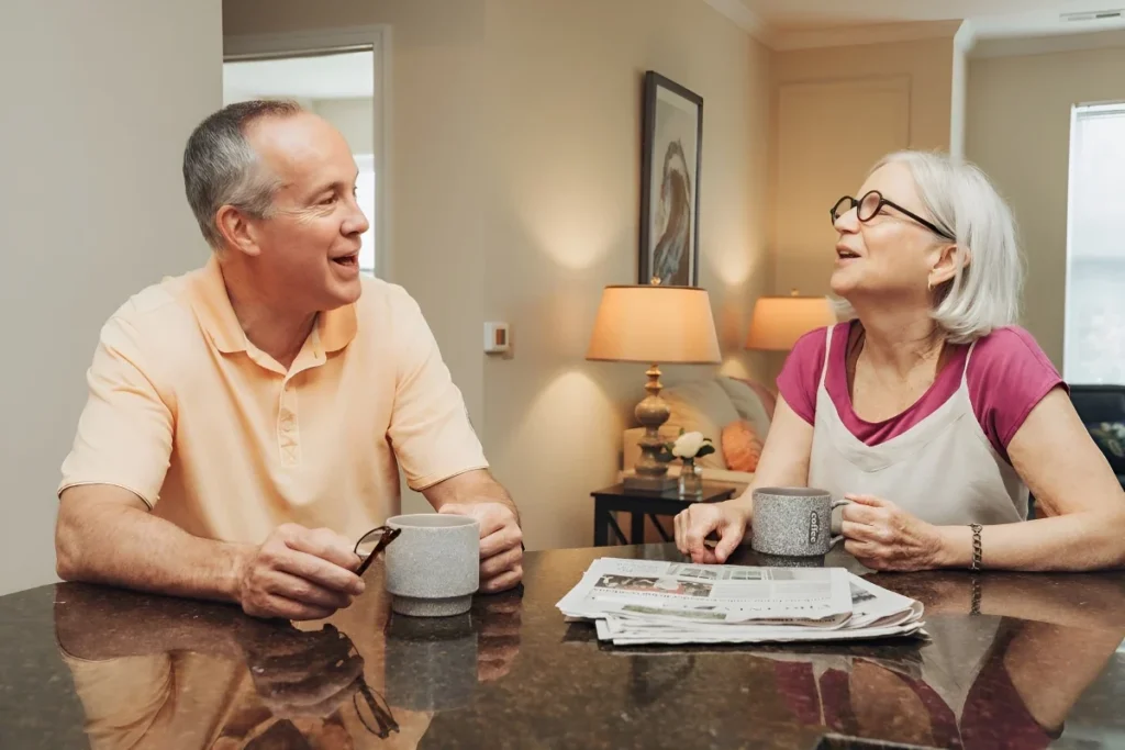 Older man and woman smiling over coffee and a newspaper at a table