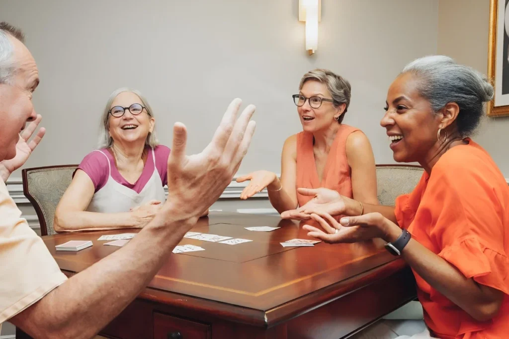 Senior adults chatting and laughing around a wooden table while playing cards