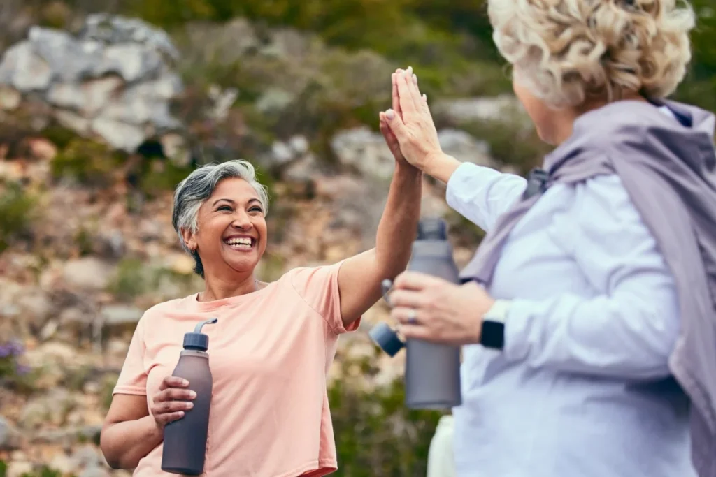 Two active older women high-fiving on a hike, one holding a water bottle