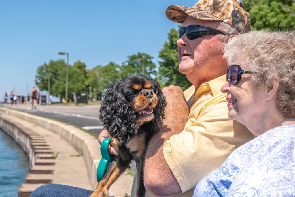 Senior couple sitting by the water holding a small dog