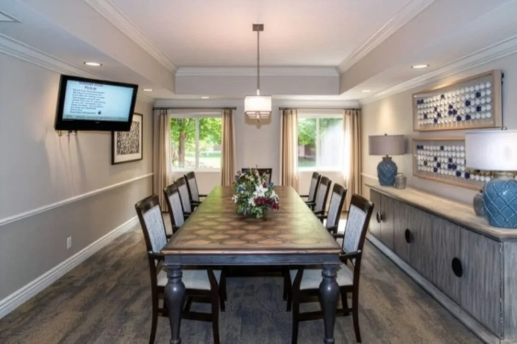 Dining room with a long wooden table set for a group, a wall-mounted TV and a sideboard