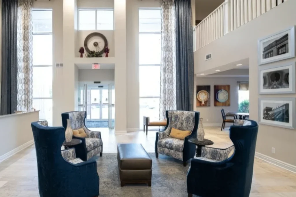 Lobby lounge with blue armchairs, a bench, framed photos on the wall and tall windows