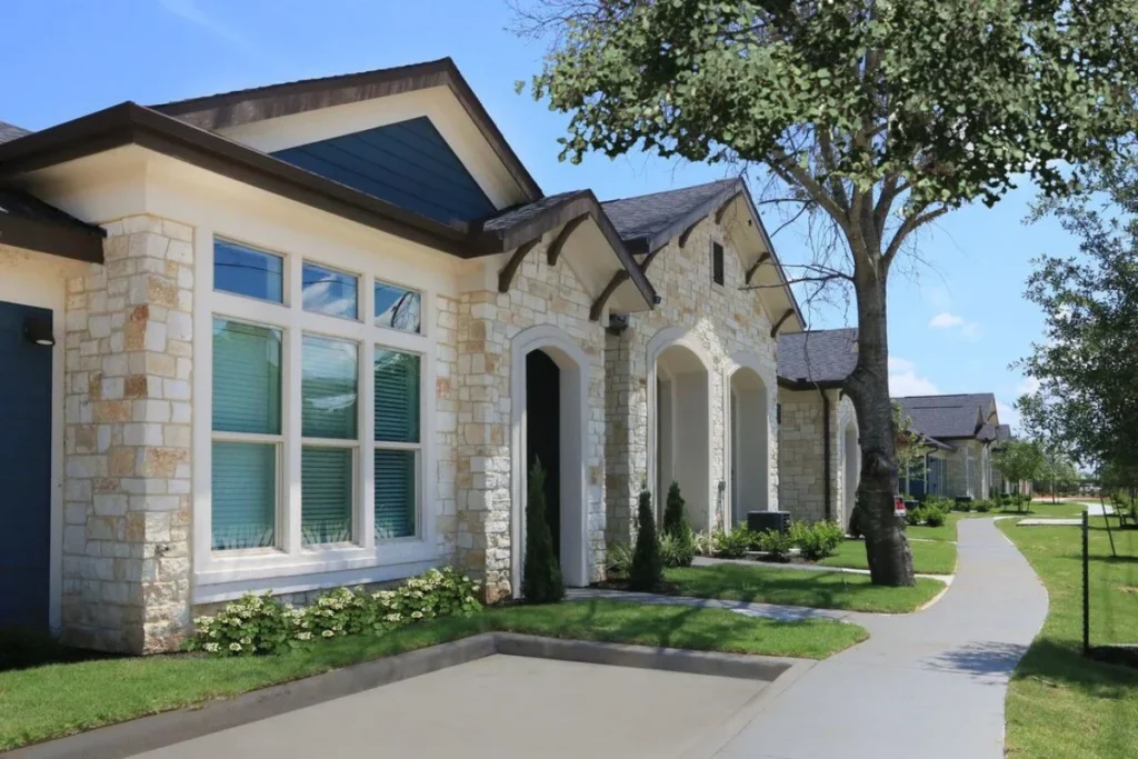 Stone-accented single-story home with tall windows beside a curving walkway and lawn