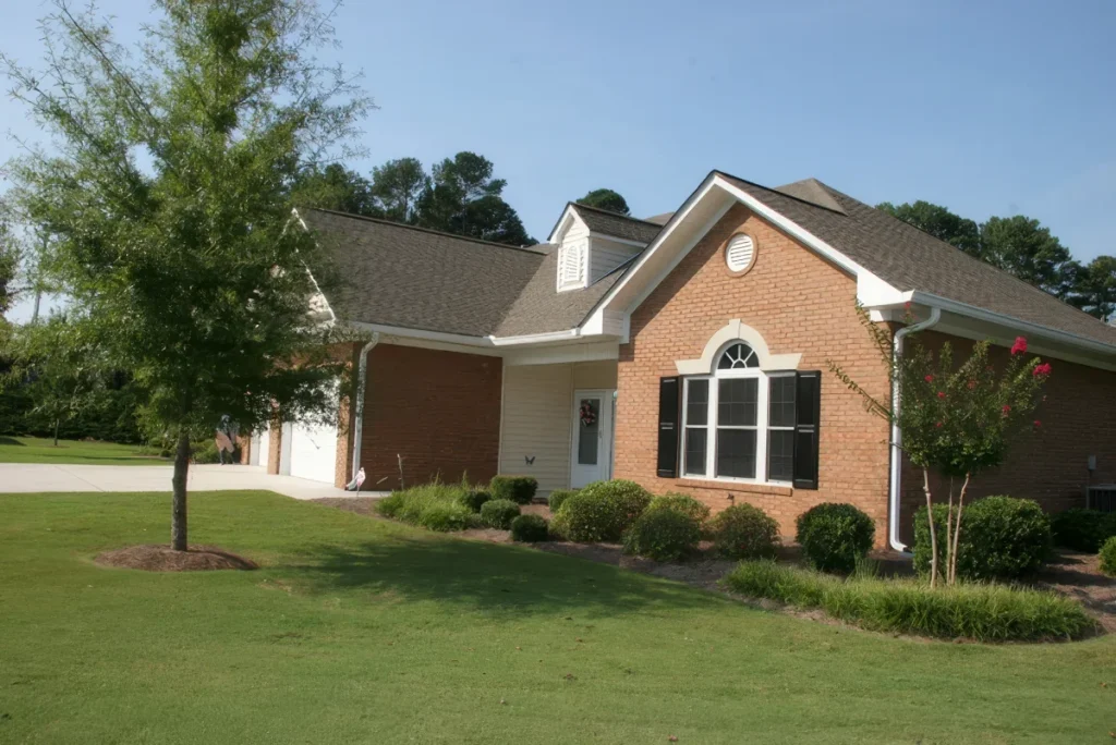 Brick home with an arched window and a landscaped lawn beneath a large tree