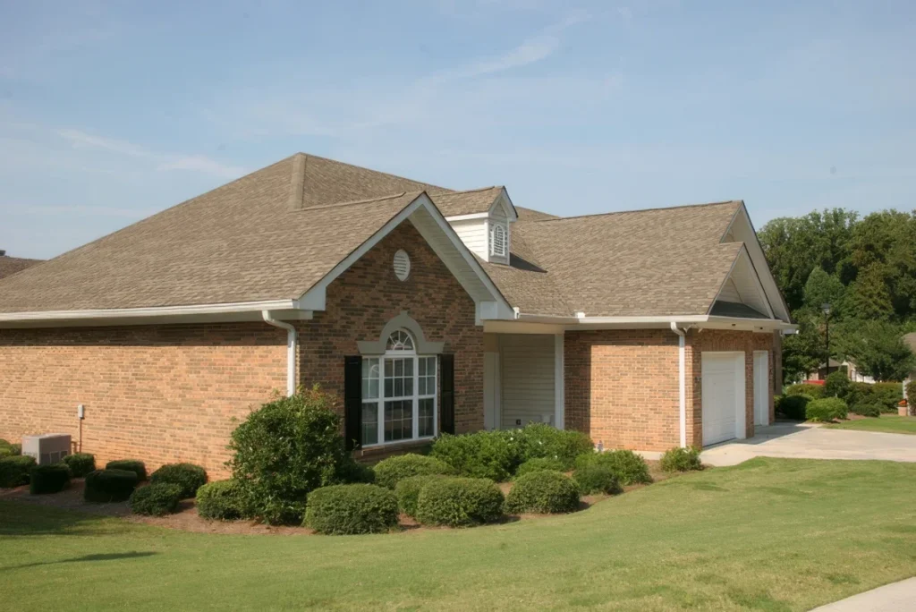 Brick home with a hip roof, landscaped shrubs and a lawn under a blue sky