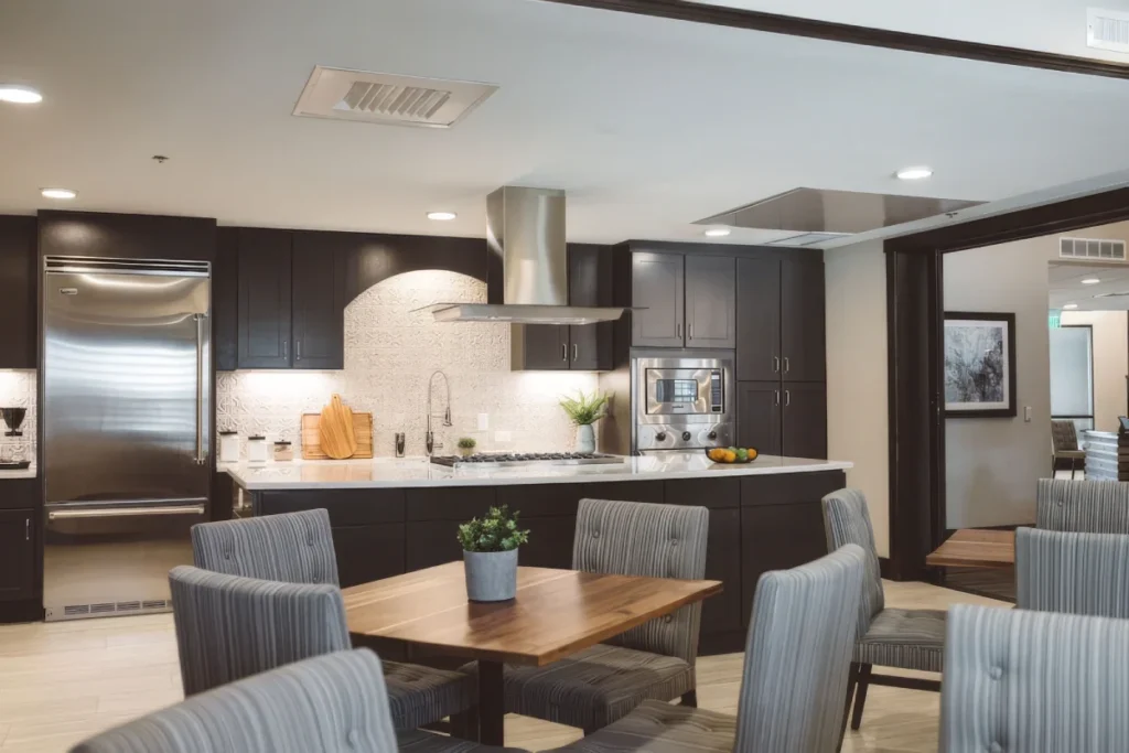 Open kitchen with dark cabinets, a stainless steel hood and a dining table with gray chairs