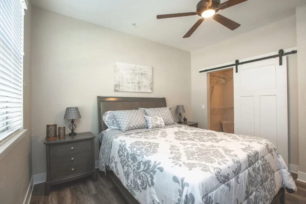 Bedroom with a floral bedspread, nightstands, a ceiling fan and a sliding barn door