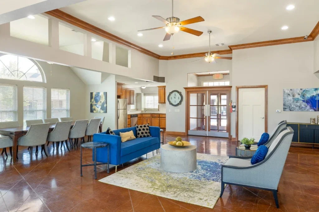 Open living and dining area with a blue sofa, a ceiling fan and a long table under a vaulted ceiling