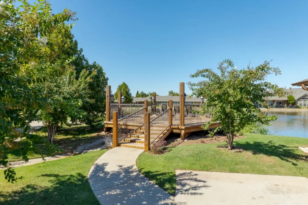 Wooden dock and walkway beside a pond, with grassy paths and trees