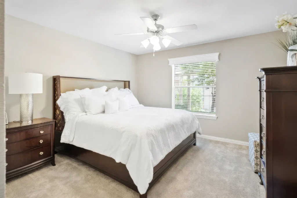 Bedroom with a white bed, a wooden headboard, a nightstand and a ceiling fan