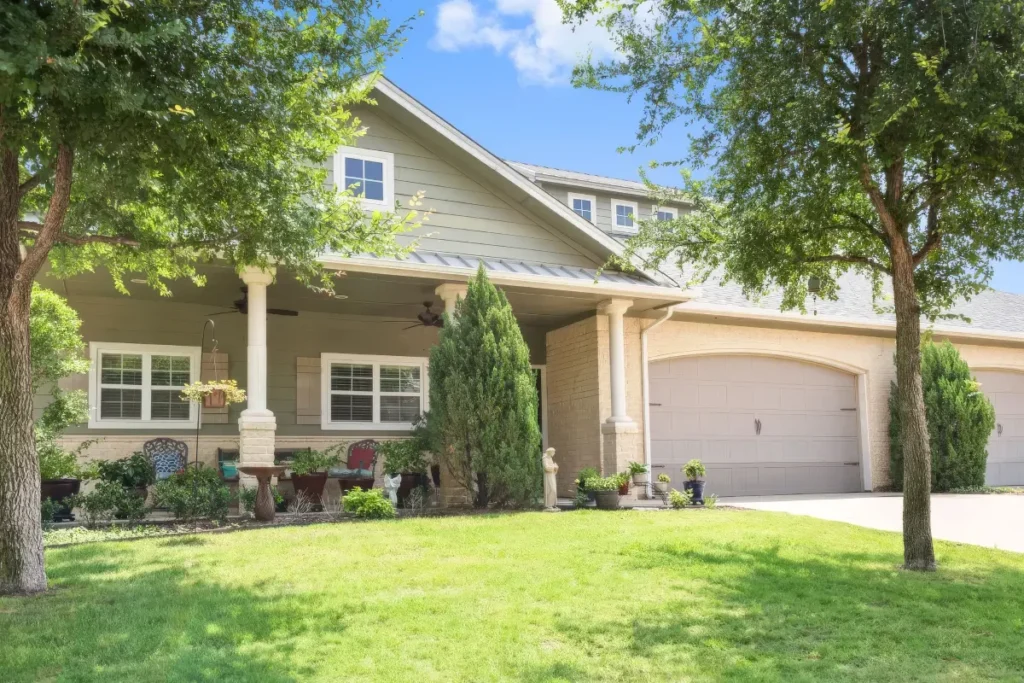Single-story home with a covered porch and garage, framed by large trees and a lawn