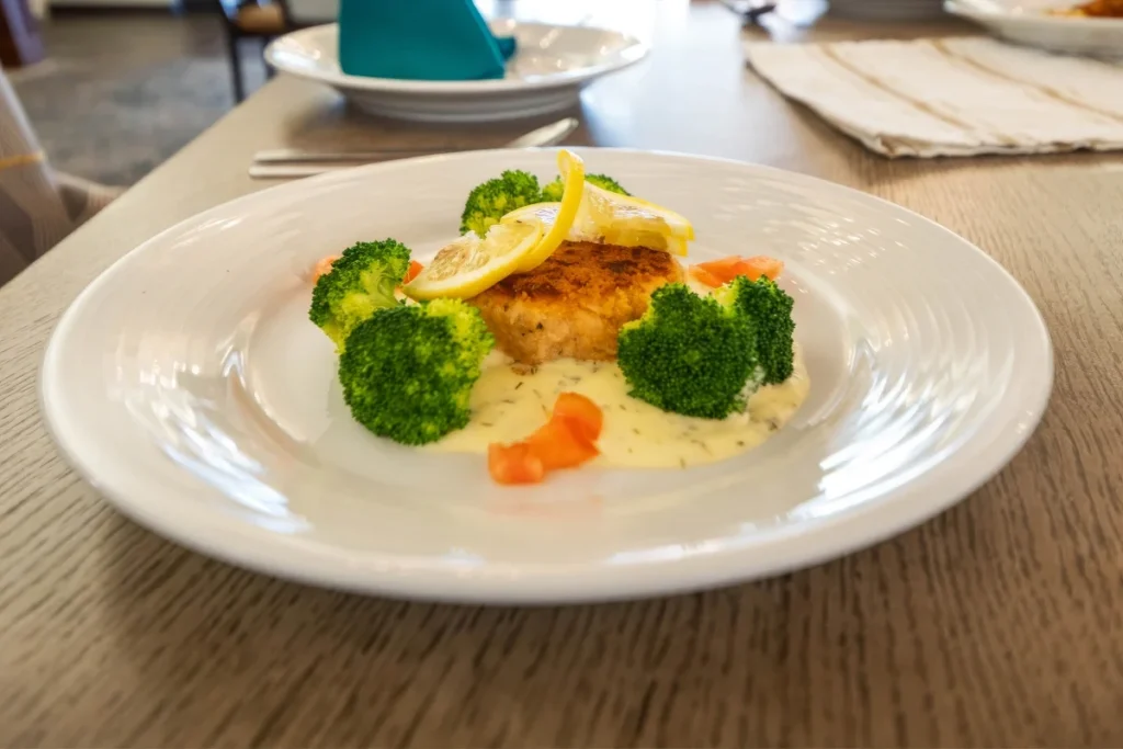 Plate of baked fish topped with lemon, served with broccoli and carrots