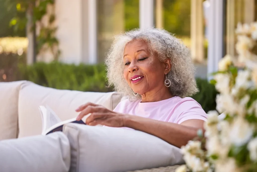 Older woman with curly gray hair relaxing on an outdoor sofa with a book