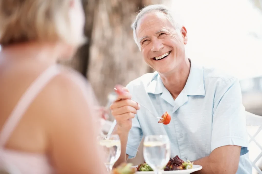 Smiling older man in a light blue shirt eating a salad at an outdoor table