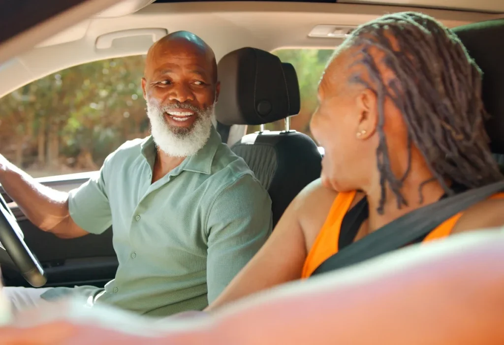 Smiling older man driving a car while a woman in the passenger seat smiles at him