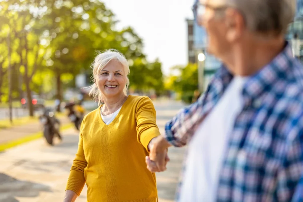 Smiling woman in a yellow sweater walking hand in hand with a man on a tree-lined street