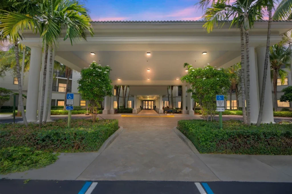 Covered building entrance with palm trees and landscaped walkways at dusk